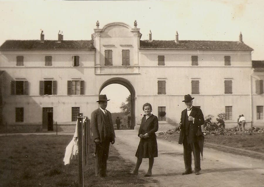 Cascina Pizzavaccaの農園の建物と、その前に立つ正装した人々の歴史写真